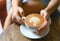 Women`s hand holding a cup of coffee latte heart shaped leaves texture on wooden table