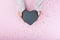 Women`s hands hold a gift in the form of a black heart on a beautiful pink background with sequins