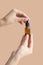 Women& x27;s hands hold mock-up of glass dropper bottle on beige background. Close-up, place to copy, vertical image. Concept