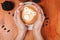 Women`s hands holding a Cup of coffee with a painted Teddy bear latte art. Vintage color. Coffee shop concept