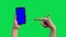 Women`s hands with the phone are raised in the frame on a green background. In one hand, a phone with a blue screen and