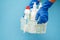 Women`s hands in protective glove with bottles of glass cleaner in basket on blue background