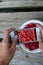 Women`s hands take close-up photos of fresh forest raspberries in a plate on a gray wooden table