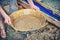 Women`s hands with a tray for the extraction of gold sand in US. Woman gold digger in the American wild West. Washing sand in