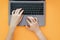 Women`s hands type the text on the keyboard of the laptop on the orange background, the top view