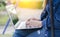 Women`s hands wearing denim clothes, sitting in the garden, working independently with modern laptops.