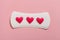 Women`s health care, daily or menstrual pad with red hearts as blood drops on rose background. female critical days