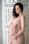 Women`s health and pregnancy. A beautiful pregnant woman in a tender pink dress is standing near an openwork wooden