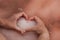 Women`s heart-shaped hands hold pink salt on water surface of unique pink lake. Original color of lake is given by halophilic