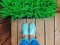 Women`s legs in mint sneakers on terrace board with artificial grass in flowerpot