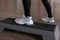 Women`s legs in stylish sporty white sneakers stand on the platform steps in the gym. Young woman trains in a fitness studio.