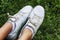 Women`s legs in white sneakers on the grass in a summer park. Rest and walks in nature. Close-up