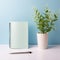 Women\\\'s Office Desk in Minimalist Style: Light Blue and Silver Notebooks, Pen, and Green Plant in Vase - Organized Workspace