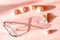 Women`s pink sunglasses with metal frame cast a long shadow on the pink surface with seastar and seashell.