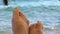 Women`s toes and feet against the background of the sea, the rays of the sun on the waves, beach vacation, summer resort