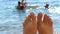 Women`s toes and feet against the background of the sea, the rays of the sun on the waves, beach vacation, summer resort