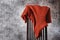 Women`s wool knitted terracotta sweater casually thrown over the back of wooden chair against gray wall. Copy space