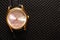 Women& x27;s wristwatch. Gold metal watch. Black fabric background pattern. Clock hands.