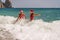 Women Santa hats ocean play. Seaside, beach daytime, enjoying beach fun. Two women in red swimsuits and Santa hats are