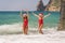 Women Santa hats ocean play. Seaside, beach daytime, enjoying beach fun. Two women in red swimsuits and Santa hats are