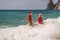 Women Santa hats ocean play. Seaside, beach daytime, enjoying beach fun. Two women in red swimsuits and Santa hats are