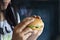 Women see hamburger in hand on dark background, junk food concept