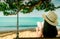 Women sit and reading a book on swings under the tree by the sea. Back view of Asian woman with straw hat relax and enjoy