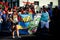 Women in vivid costumes carry big group flag by city street at dominican carnival