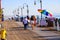 Women walking along a long brown wooden pier with tall curved light posts along the edge of the pier