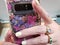 Women with yellow nails and rings holding a smart phone with  a purple and pink flower case