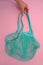 Womens hand takes cotton green mesh bag on pink paper background