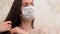 Wonderful Caucasian ill girl with long dark brown hair wear blue protective medical face mask, take a thermometer out