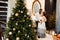Wonderful couple stand near Christmas tree at home, caring husband hug pregnant wife, young family enjoy happiness