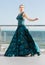 Wonderful elegant lady in a long waving emerald dress, posing near a bright blue sea. The beautiful girl on vacation on the sea.