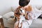 Wonderful girl with trendy short hairstyle kissing beagle dog while sitting on gray sofa. Indoor portrait of amazing