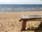 A wonderful place to stay. Wooden gray bench on a sandy beach near a tree overlooking the sea. Sunny day. Gulf of Finland