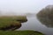 Wonderful rural landscape. Quiet river on a foggy spring morning. Medium and tall trees are shrouded in fog.