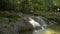 Wonderful scenery of water stream flowing from cascade through the rock into a small natural pond under sunlight.