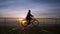 Wonderful sunrise or sunset above ocean. Silhouette of young stylish girl cycling on vintage bike on wooden embankment