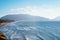 Wonderful view of beach with buildings seashore coastline, sea waves, mountains surrounded by clouds on sunny windy day.