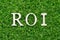 Wood alphabet in word ROI Abbbreviation of Return on Investment on artificial green grass background