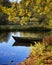 Wood boat is landing near the shore of the pond. Lush foliage are reflected in the calm water surface