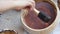 A wood craftsman is painting a teak wood bowl with brown wood stain