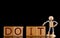 Wood cube block with word â€œDO ITâ€ and Wooden Stick Figure standing on Black Background.