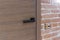 Wood entry door with black handle and industrial brick wall, close up