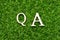 Wood letter in word QA abbreviation of quality assurance or question and answer on green grass background