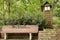 A wood park bench engraved with an inspirational quote along a stone retaining wall, shrubs, trees and a wood light house