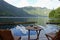 A wood table and two chairs on a deck overlooking the calm scenic ocean with forest and mountains in the background