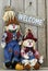 Wood welcome sign hanging on wooden fence by boy and girl scarecrows