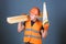 Woodcraft concept. Man, handyman in helmet, hard hat holds handsaw and wooden beams, grey background. Carpenter